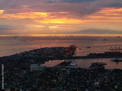 Manila's lively port area at sunset, featuring cargo ships dotted across the horizon against a dramatic sky with colorful clouds, and city lights twinkling below