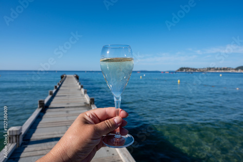 Summer time in Provence, hand with glass of cold champagne cremant sparkling wine on famous Pampelonne sandy beach near Saint-Tropez in sunny day, Var department, France, beach club party photo