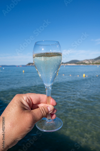 Summer time in Provence, hand with glass of cold champagne cremant sparkling wine on famous Pampelonne sandy beach near Saint-Tropez in sunny day, Var department, France, beach club party photo