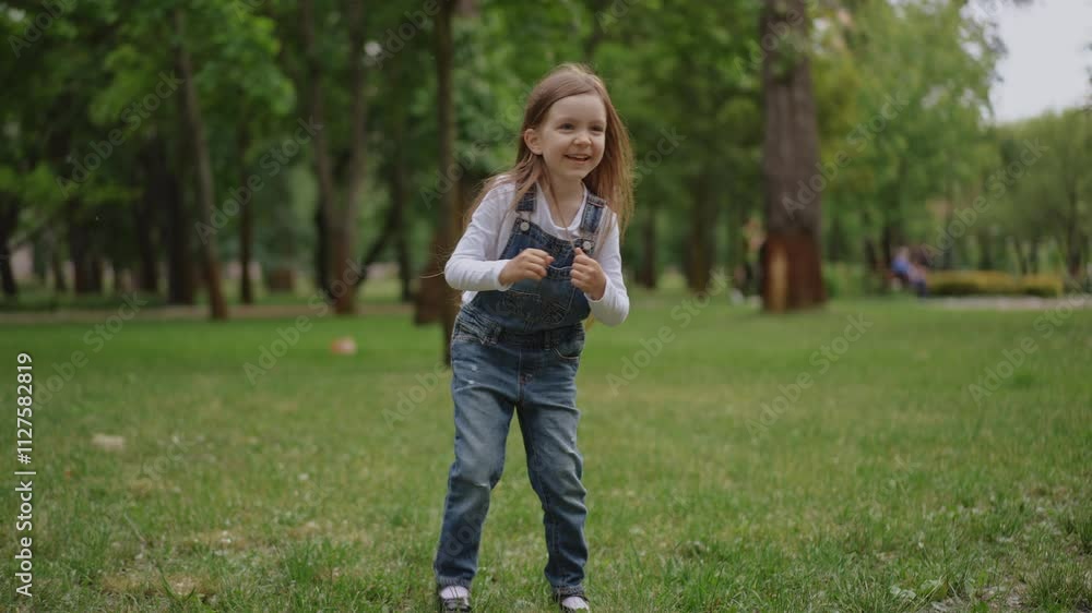 A joyful child dressed in colorful overalls is playing happily in a vibrant, lush green park full of trees and nature A joyful child dressed in colorful overalls is playing happily in a vibrant, lush green park full of trees and nature