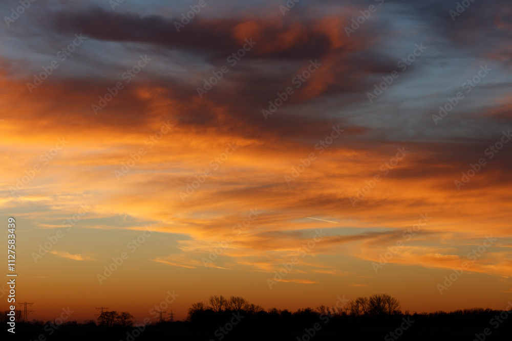 Sunset sky ablaze with fiery oranges and yellows, silhouetted trees line the horizon. Dramatic clouds fill the sky. Sunset sky ablaze with fiery oranges and yellows, silhouetted trees line the horizon. Dramatic clouds fill the sky.