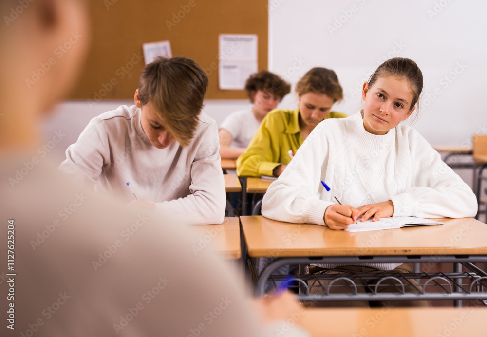 Portrait of teenage school girl and boy sitting together in classroom during lesson in secondary school Portrait of teenage school girl and boy sitting together in classroom during lesson in secondary school