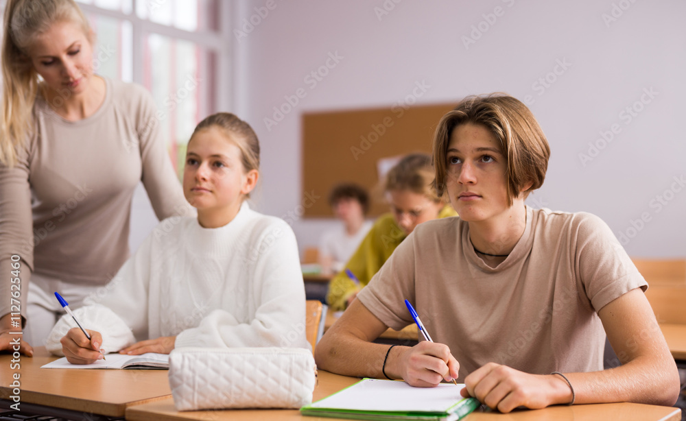 Fototapeta premium Teenage girl and boy sitting together at desk and doing tasks in classroom..