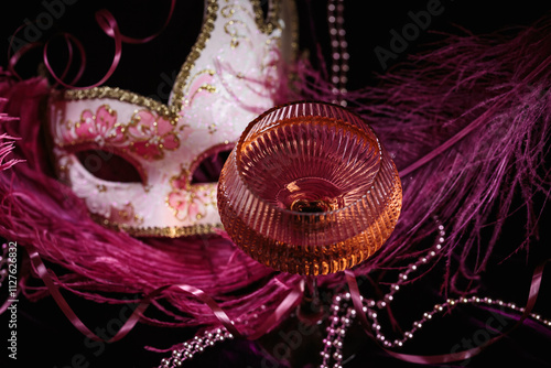 Masquerade ball holiday background. Glass of rose champagne, Venetian carnival mask and feathers on dark burgundy velour background photo