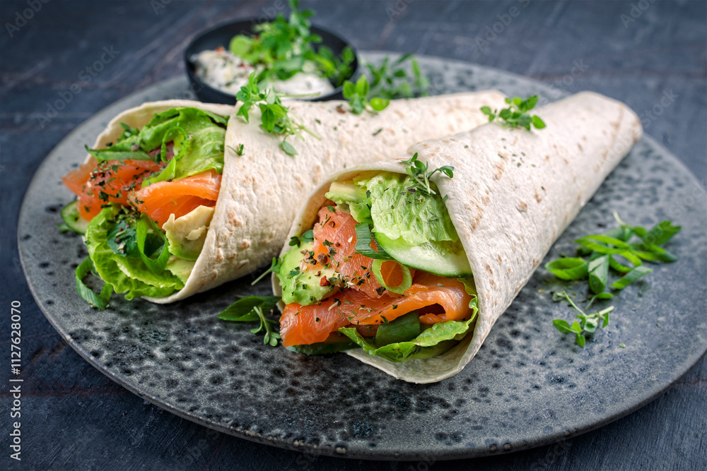 Italian style wrap piada tortilla with cured graved salmon, salad and avocado served as close-up with sour cream dressing dip on a Nordic Design plate Italian style wrap piada tortilla with cured graved salmon, salad and avocado served as close-up with sour cream dressing dip on a Nordic Design plate