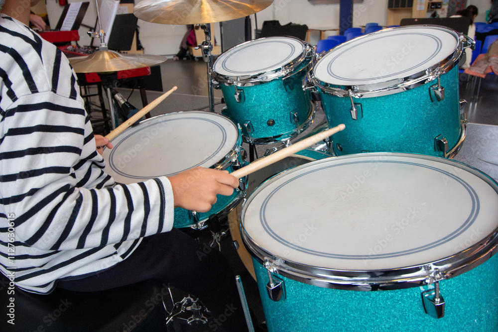 Obraz premium Child Playing Turquoise Drum Set: Hands Holding Drumsticks in a Music Classroom