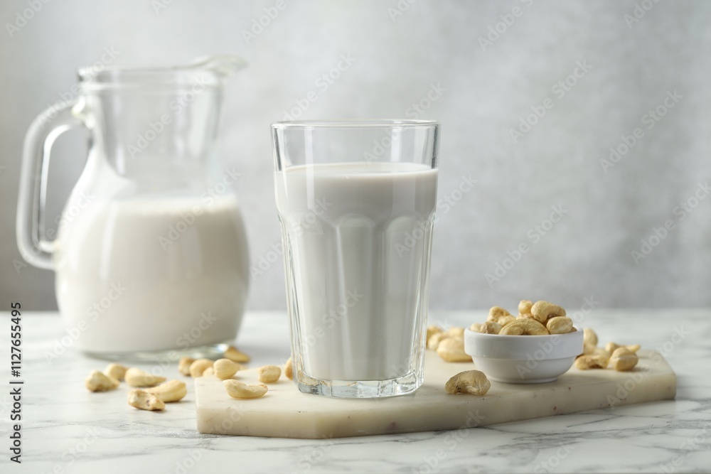 Fresh cashew milk in glass and nuts on white marble table against light background, closeup Fresh cashew milk in glass and nuts on white marble table against light background, closeup