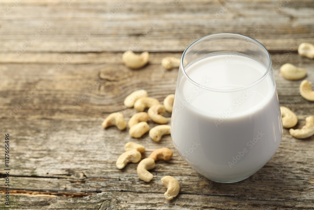 Fresh cashew milk in glass and nuts on wooden table, closeup. Space for text Fresh cashew milk in glass and nuts on wooden table, closeup. Space for text