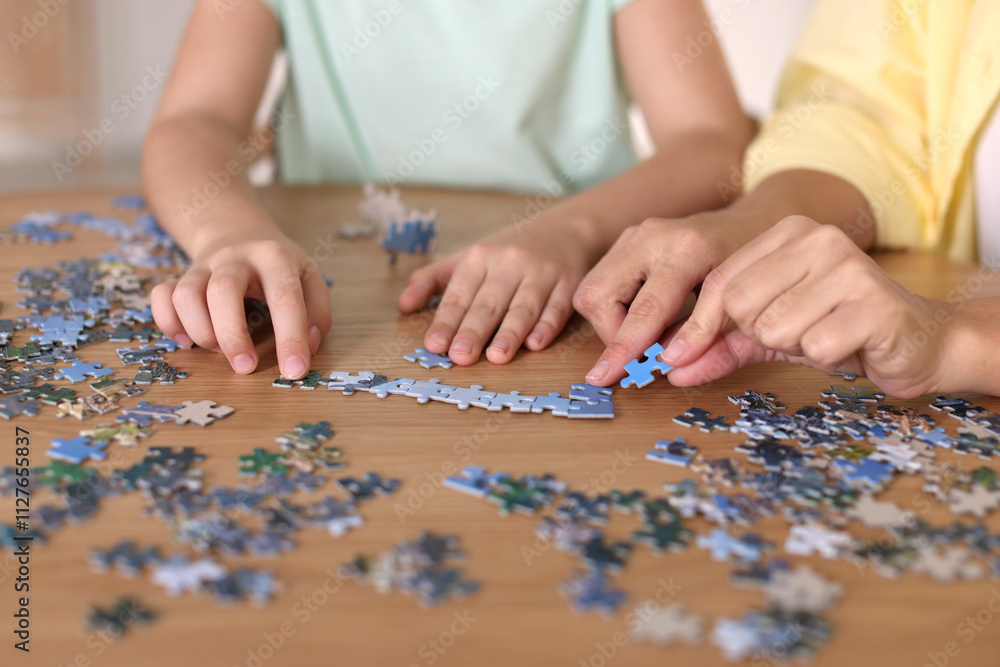 Mother and her daughter solving puzzle together at wooden table indoors, closeup Mother and her daughter solving puzzle together at wooden table indoors, closeup