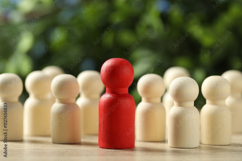 Human resources concept. Red figure in front of wooden ones on table against blurred background, closeup. Space for text Human resources concept. Red figure in front of wooden ones on table against blurred background, closeup. Space for text