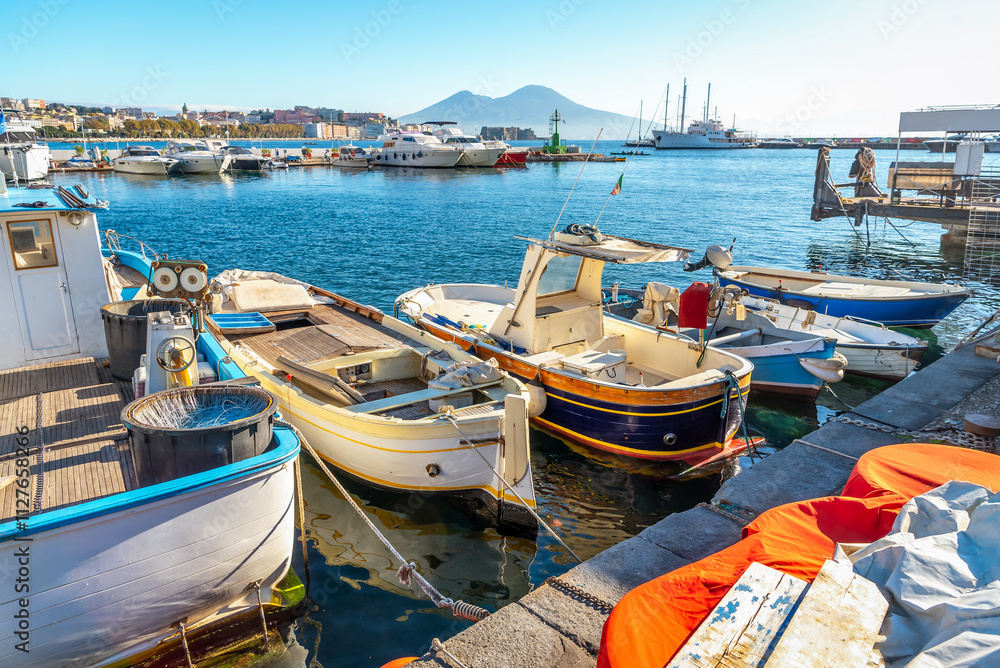 Obraz premium Fishing boats at the pier in the port of Naples on a sunny day with Mount Vesuvei in the background