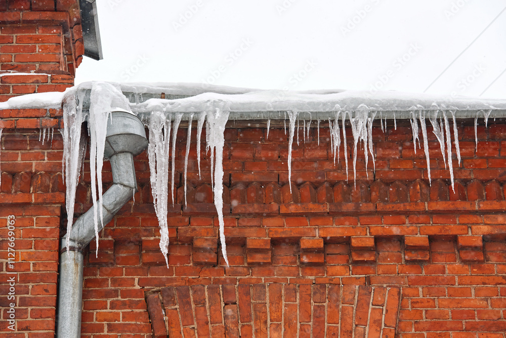 Big sharp icicles on roof of residential house, icy drain pipe. Icicles hanging on roof, risk for pedestrians in winter season. Icicle on rooftop of the building. Icicles hanging from the roof