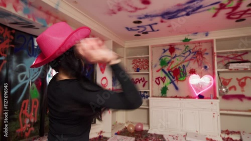 A young woman wearing a pink cowboy hat throws a red paint bomb at a vandalized wall. photo