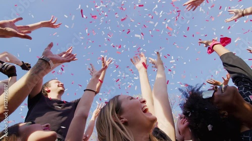 Shot of a lot of people reaching up to the blue sky as confetti comes raining down. photo