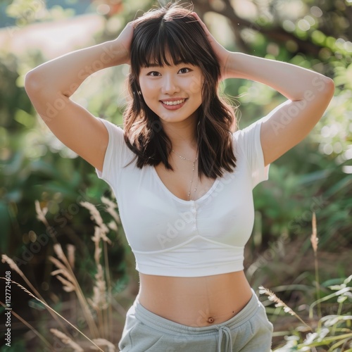 Asian woman in a white sports bra stands outdoors in sunlit field. The morning sunlight creates a soft rim light, highlighting her natural beauty and athletic form.