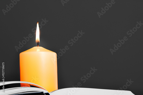 Candle is lit on an open book. Book with black candle on the background. Book with a burning candle on the background blurred. A book burning in a blurred background with a black lifestyle candle. photo