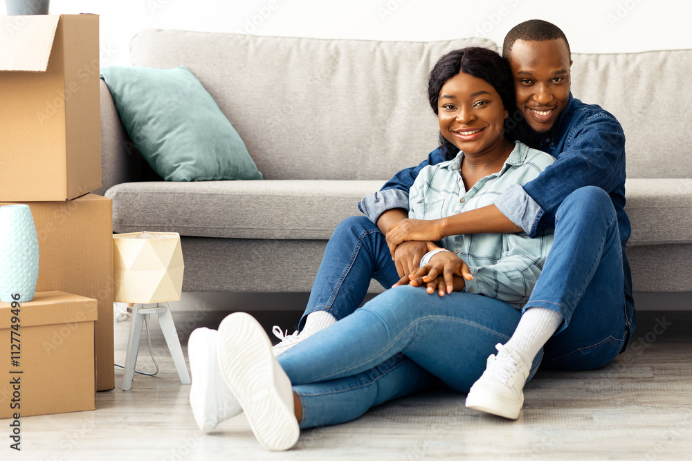 Happy african american couple sitting on floor in room with cardboard boxes on moving day, cheerful black spouses embracing and smiling to camera, celebrating relocating to new apartment, free space Happy african american couple sitting on floor in room with cardboard boxes on moving day, cheerful black spouses embracing and smiling to camera, celebrating relocating to new apartment, free space