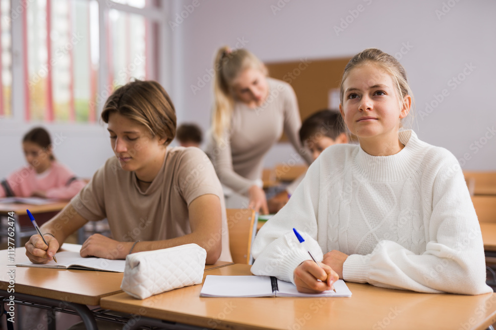 Teenage girl and boy sitting together at desk and doing tasks in classroom. Teenage girl and boy sitting together at desk and doing tasks in classroom.