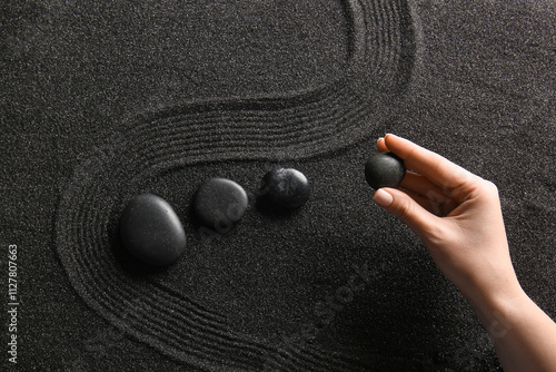 Photography Female hand and stones on black sand with lines. Zen concept