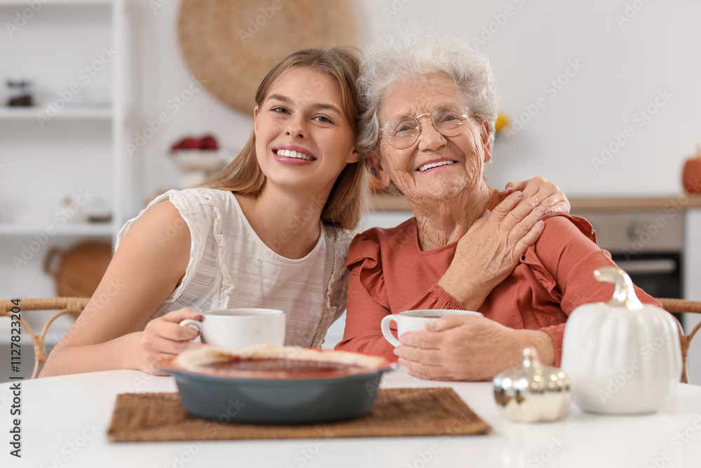 Young woman with her grandmother and tasty pie drinking tea at table in kitchen Young woman with her grandmother and tasty pie drinking tea at table in kitchen