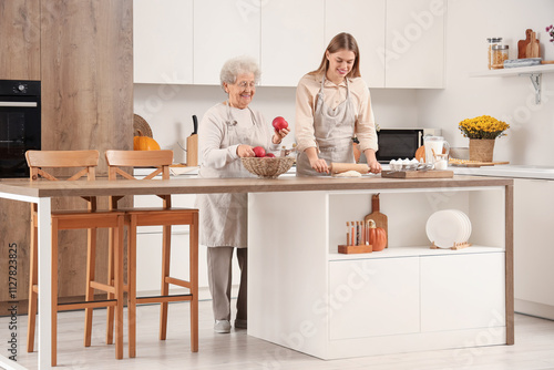 Senior woman with apples and her granddaughter rolling out dough in kitchen