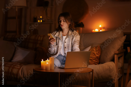 Obraz na plátně Young woman with laptop using mobile phone at home during blackout
