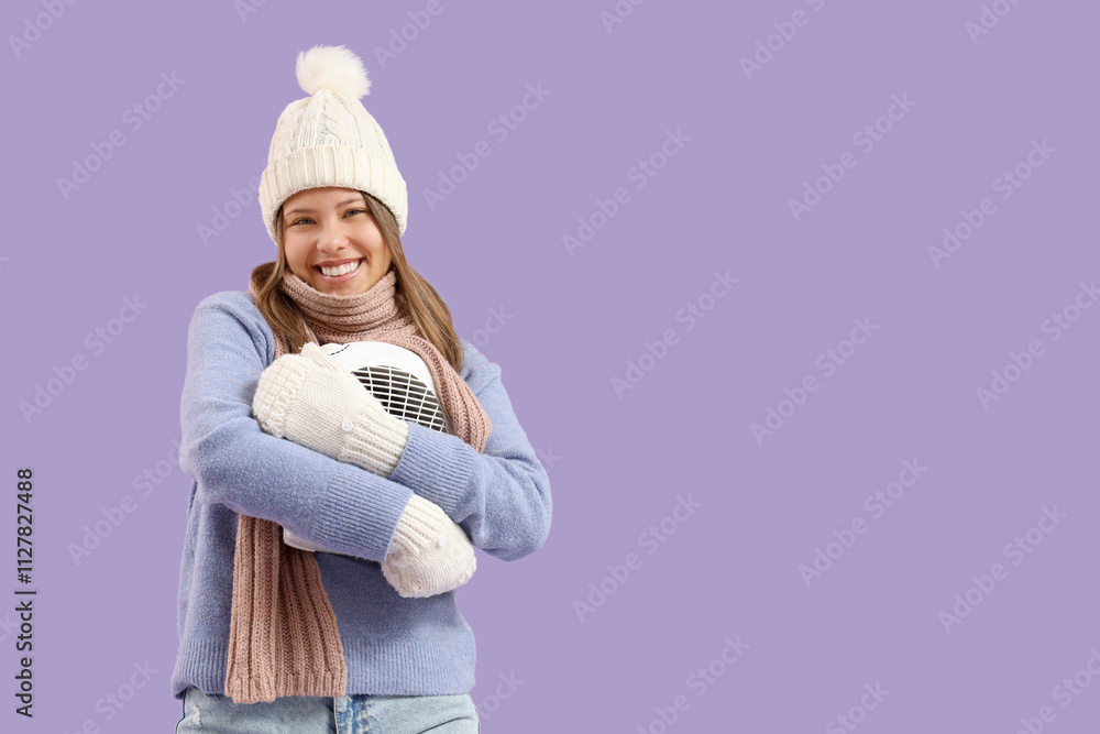 Young woman in winter clothes with electric fan heater on lilac background Young woman in winter clothes with electric fan heater on lilac background