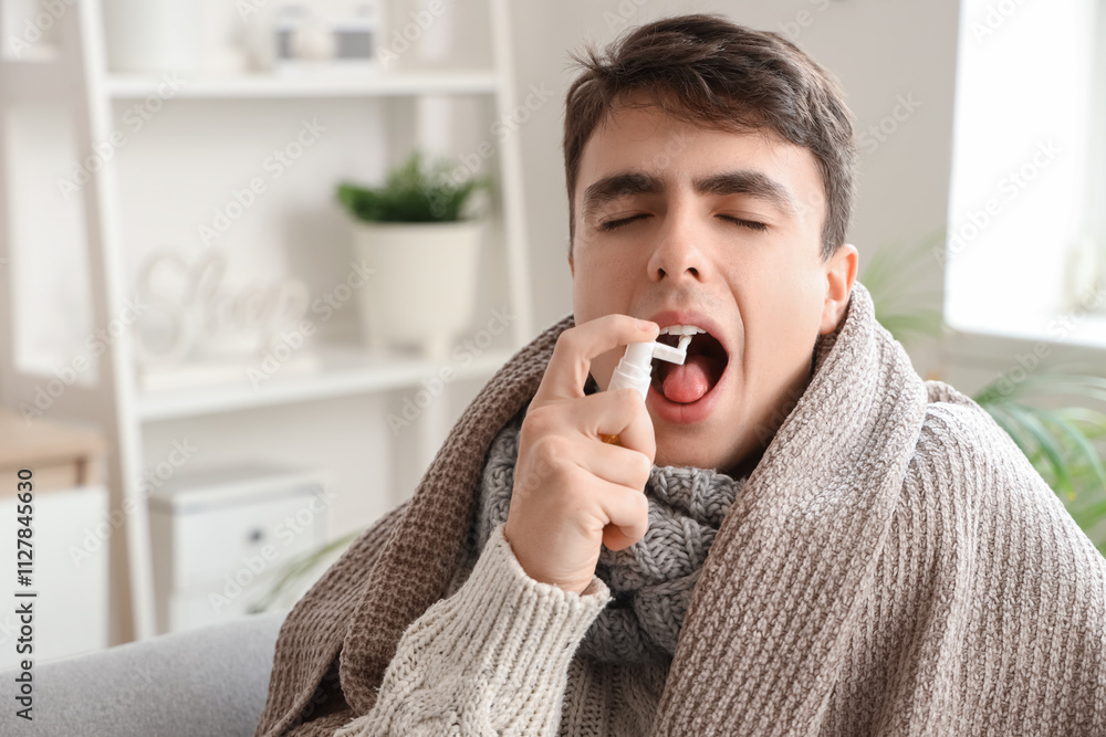 Fototapeta premium Ill young man with plaid spraying his sore throat at home, closeup