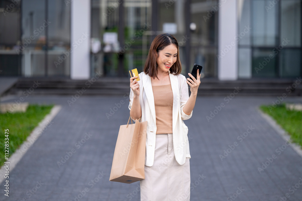 Fototapeta premium A woman is holding a shopping bag and a cell phone