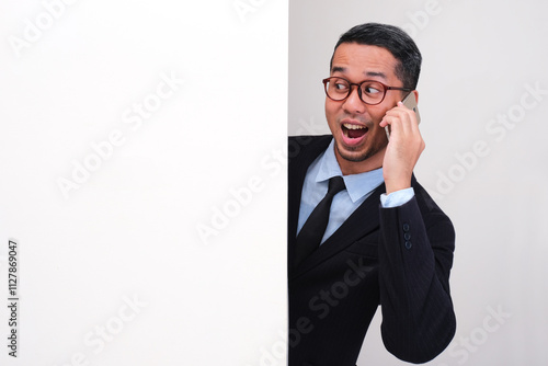 A businessman peeking out behind wall while talking on the phone with happy face photo