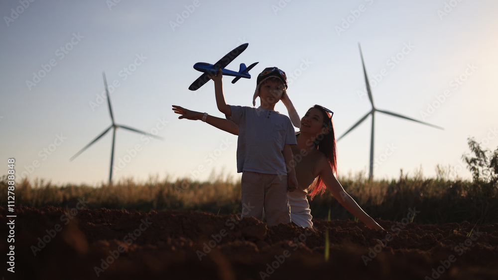 A little boy is playing with his toy airplane in a field of windmills learning green renewable energy, and hanging out with his mom as the sun sets. A little boy is playing with his toy airplane in a field of windmills learning green renewable energy, and hanging out with his mom as the sun sets.