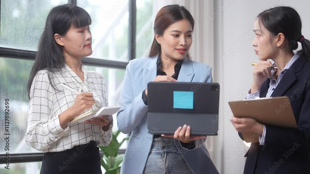 Three women are standing in a room, one of them holding a laptop. They are all dressed in business attire and appear to be discussing something important Three women are standing in a room, one of them holding a laptop. They are all dressed in business attire and appear to be discussing something important