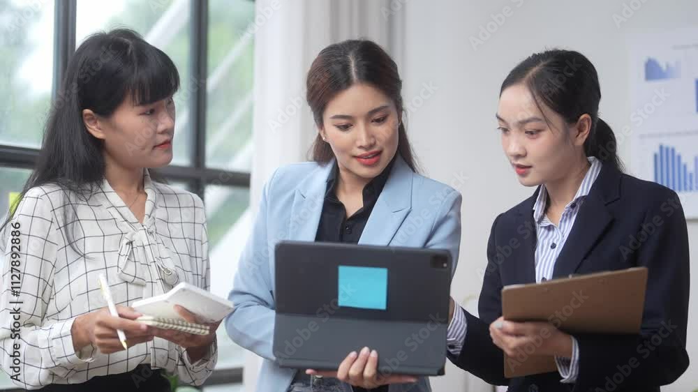 Three women are sitting around a table, one of them holding a tablet. They are discussing something important, and the woman with the tablet is pointing at it. Scene is serious and focused Three women are sitting around a table, one of them holding a tablet. They are discussing something important, and the woman with the tablet is pointing at it. Scene is serious and focused