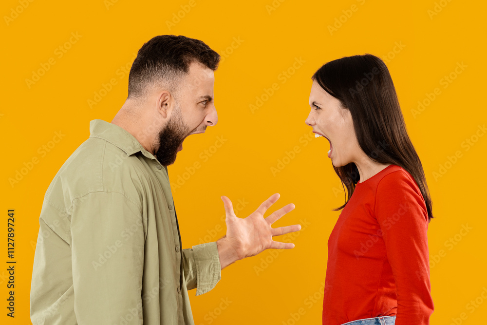 A young married couple stands facing each other, demonstrating a strong emotional conflict. The man raises his hand to express frustration while the woman passionately responds. A young married couple stands facing each other, demonstrating a strong emotional conflict. The man raises his hand to express frustration while the woman passionately responds.