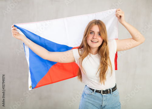 joyous girl in arms raised above head holds canvas of national flag of Czechia. concept of unity and self-determination. Gray background photo