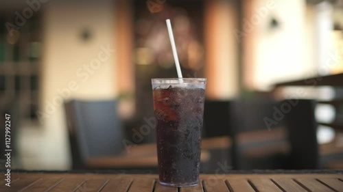 Close-up of refreshing glass of soda with ice and straw on wooden table in cozy indoor dining setting glass of soda with ice and straw glass of soda in cozy indoor dining setting photo