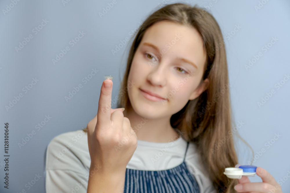 Portrait of positive cheerful little girl care eye hold transparent contact lens isolated over gray color background Portrait of positive cheerful little girl care eye hold transparent contact lens isolated over gray color background