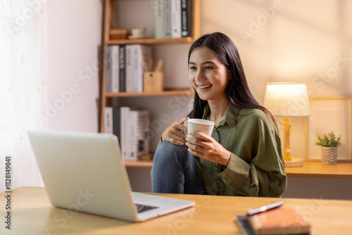 Beautiful young Asian woman working with laptop computer in home kitchen. Work at home. Remote studying E-learning, Watching online education, Webinar at house
