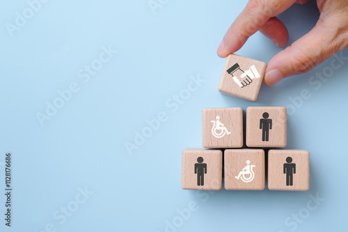 For supported employment and inclusive workplace concept. wooden cube blocks with disabled person and men icons, hand place handshake sign on top on blue background
