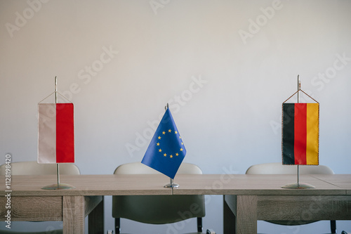 Das Bild zeigt drei Tischflaggen, die auf einem hellen Holztisch angeordnet sind. Von links nach rechts sind die Flaggen von Polen, der Europäischen Union und Deutschland zu sehen. 