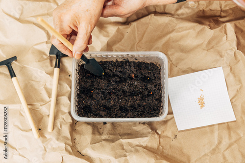 Kraft paper background, fertile soil and garden tools, top view. Hands planting seeds