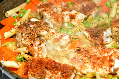 Fried cod pieces are cooked in a frying pan together with vegetables. photo