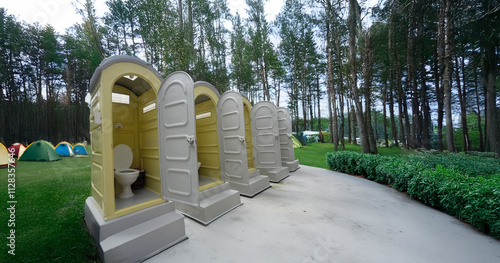 Portable toilet placed on a spacious camping ground surrounded by tents and outdoor scenery,