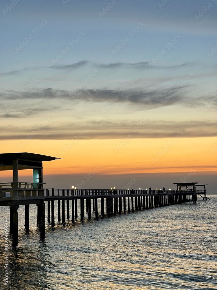Fototapeta premium pier extending from the beach into the ocean toward orange sunrise.