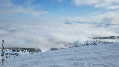 winter view of snow-covered mountains. Ski slope. Ski resort. Mountains in clouds, clear day, forest