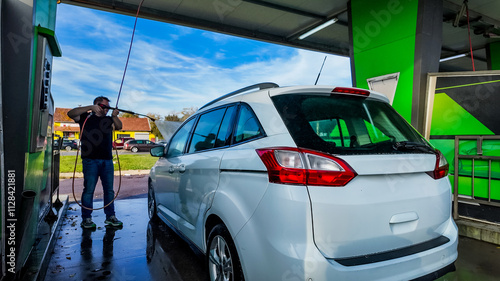 Obraz na plátně A Caucasian man washing a white car at a self-service car wash, emphasizing clea