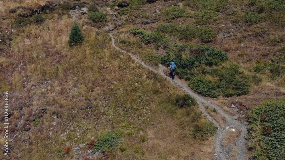 Aerial: Backpacker with heavy load hikes slowly up mountain trail