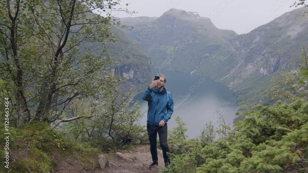 Man takes a selfie while hiking above Norway's Geirangerfjord on a cloudy day Man takes a selfie while hiking above Norway's Geirangerfjord on a cloudy day