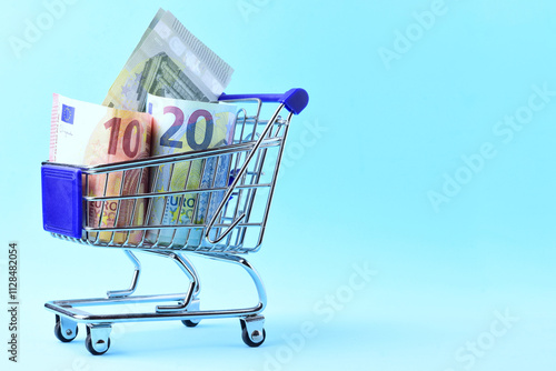 Euro bills of different amounts in a shopping cart and blue background, copy space.