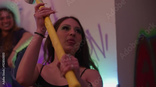 Cool young woman smashing a wall with a hammer at a house party full of people. photo